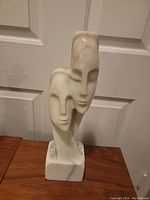 Front and side views of 16-inch tall alabaster or marble sculpture of two abstract intertwined faces on rectangular base, showing natural stone veining and smooth finish.