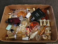 Top view of a large cardboard box filled with many perfume bottles and perfume samples. Bottles vary in size and design, some nearly full and others partially empty.