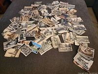 Wide view of a large pile of vintage postcards spread on a surface, displaying mainly architectural and city images.
