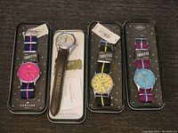 Four new Fossil watches displayed in original tin cases, three with colorful fabric straps and one with a leather strap.