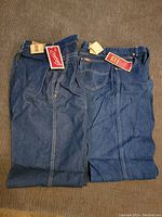 Two pairs of folded vintage Lee jeans on a carpeted surface showing the front and back sides with attached tags.
