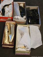 Top-down view of five pairs of women's shoes in separate boxes wrapped partly in tissue paper showing various styles including metallic gold flats, black pointed flats, and black strappy sandals.