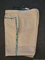 Tan Ralph Lauren pants folded showing back pocket and turquoise diamond embroidery beadwork on outer leg seam, tagged.