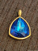 Front view of the triangular blue faceted glass pendant set in gold-tone metal.