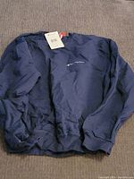 Front view of a navy blue Champion sweatshirt with embroidered logo and original tags attached, laid flat on a surface.