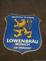 Shield-shaped Löwenbräu beer sign on a carpeted floor, fully visible with yellow lion and text.