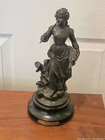 Full view of the bronze statue showing the woman standing with an ax and part of a wagon wheel on a round black base.