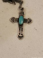 Close-up of vintage sterling silver cross pendant with oval turquoise stone set in the center, showing detailed engravings.