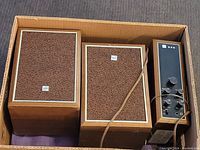 Photo showing the two wooden speakers with textured brown fabric fronts and the radio tuner/control unit with various knobs and switches in a cardboard box.