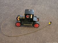Side view of the vintage black toy car with red wheels, pull string attached and molded figures inside.