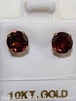 Front view of garnet stud earrings showing round deep red garnet stones in gold settings.