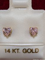 Front view of the heart-shaped pink cubic zirconia earrings set in 14k gold labeled '14 KT. GOLD' on the display stand.