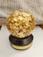 Front view of the globe showing the clear dome filled with gold leaf flakes and the black base with gold plaque marked 'BILLIONS'.