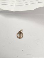 Small circular yellow gold pendant with ridged edge and letter D in center on white background.