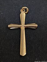 Close-up front view of 10k gold cross pendant on dark background showing faceted beveled edges and bail.