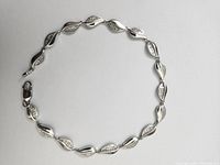 Bracelet laid flat on white background, showing alternating polished and diamond-set leaf-shaped links.