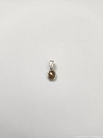Close-up image of oval-shaped pendant with brownish sapphire stone and gold bail on white background