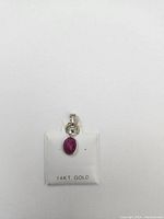 Front photo of the 14k gold pendant with oval red ruby and a small diamond above, displayed on a white 14kt gold branded card.
