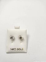 Pair of stud earrings displayed on white pad stamped “14KT. GOLD”