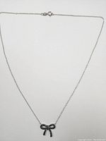 Silver necklace with bow-shaped diamond pendant laid flat on white background showing full chain and clasp