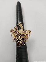 Front view of gold plated sterling silver ring styled as a peacock with 14 natural gemstones in purple and red hues.