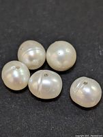 Five freshwater pearl beads of varying shape and size placed on a black background to highlight their color and surface detail.