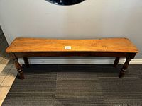 Front view of bench showing plank seat and turned legs.