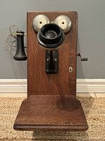 Front view of the antique wooden wall telephone with metal bells, bakelite mouthpiece and receiver hooked on the left side.