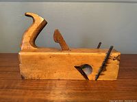 Side view of the antique wooden hand plane showing curved handle and blade mechanism, placed on wooden surface