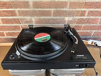 Front angled view of black Audio Reflex DD 210 turntable with a vinyl record on the platter and tonearm positioned over the record.