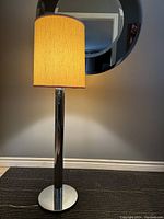 Front view of lamp illuminated to show overall design, chrome base and fabric shade