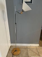 Full view of adjustable chrome floor lamp with round wooden base and white conical shade against grey wall