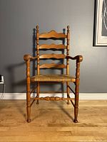 Front view of vintage farmhouse armchair showing wood frame, rush seat, and vertical wavy back slats.