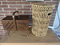 Wooden sewing box next to tall woven basket against a brick wall background