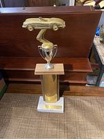 Full view of 1968 trophy showing gold-tone car figurine, silver cup with handles, gold column base, and white bottom platform on carpeted floor.