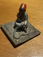 Front angled view of bronze cold painted figurine of Arab man in fez with snake on patterned base