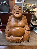 Full view of the large wooden Happy Buddha statue seated on a table, showing overall shape and posture.