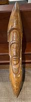 Full view of the carved wood sculpture depicting an elongated figure with an Indigenous face carved in relief.