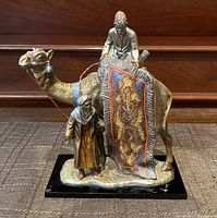 Frontal view showing full camel with rider, saddle rug, and standing figure on base