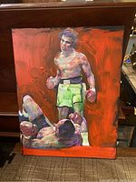 Full view of the boxing painting showing two boxers, one standing and one on the ground with a vibrant red background.