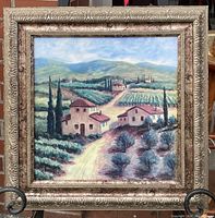 Full view of framed landscape painting featuring several houses, vineyards, cypress trees, and distant hills in a detailed gold frame.