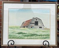 Full view of the framed watercolour painting showing the barn and grassy field with sky, displayed on a stand.