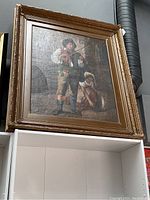 Large framed oil painting showing man playing violin with helper, set on shelf against wall.