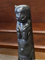 Close-up of feline-like figure at the top of the totem carving, showing carved facial features and paws.
