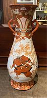Front view of tall Japanese Satsuma vase showcasing samurai warrior scene and floral motifs in red, white, and gold.