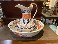 Front view of jug and basin set showing detailed hand-painted orange, blue and green floral patterns on ceramic.