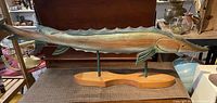 Side view of the full large wood sturgeon sculpture on the wooden base showing details of the fish body and fins.