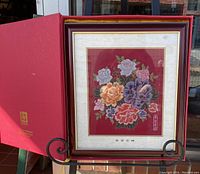 Frontal view of framed Nanjing Yunjin brocade artwork with floral peony bouquet on stand, alongside red presentation box.