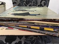 Side view of a stack of vinyl records showing various titles and worn covers