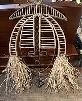 Front view of wire frame mask wrapped in raffia with raffia tassels at the sides.